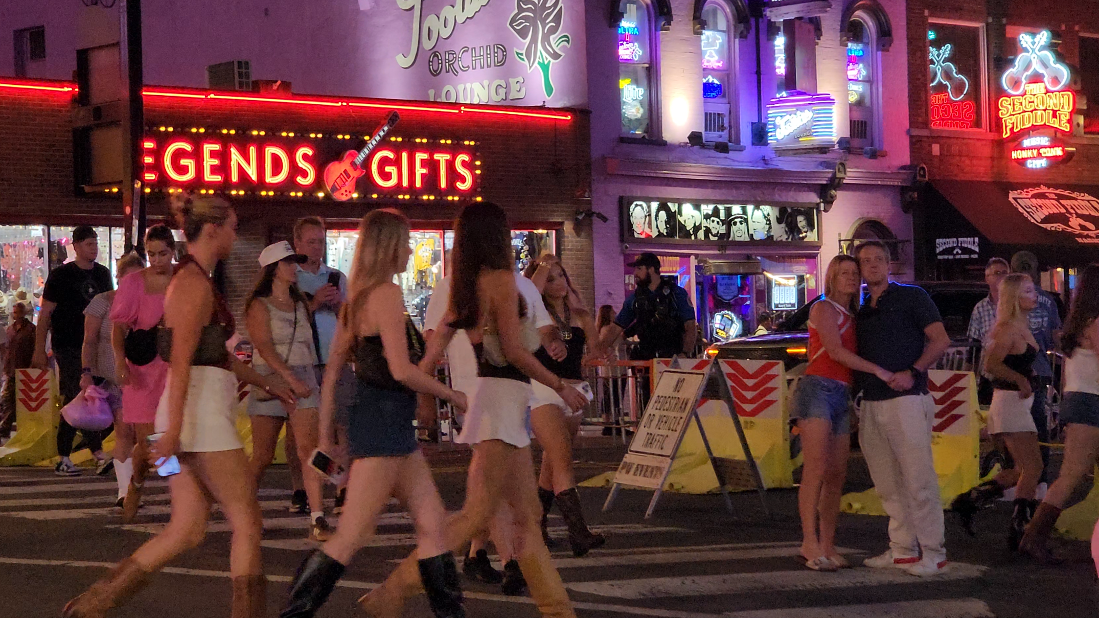 A nighttime crowd moving through a Lower Broadway crosswalk near illuminated bars and visible police presence.