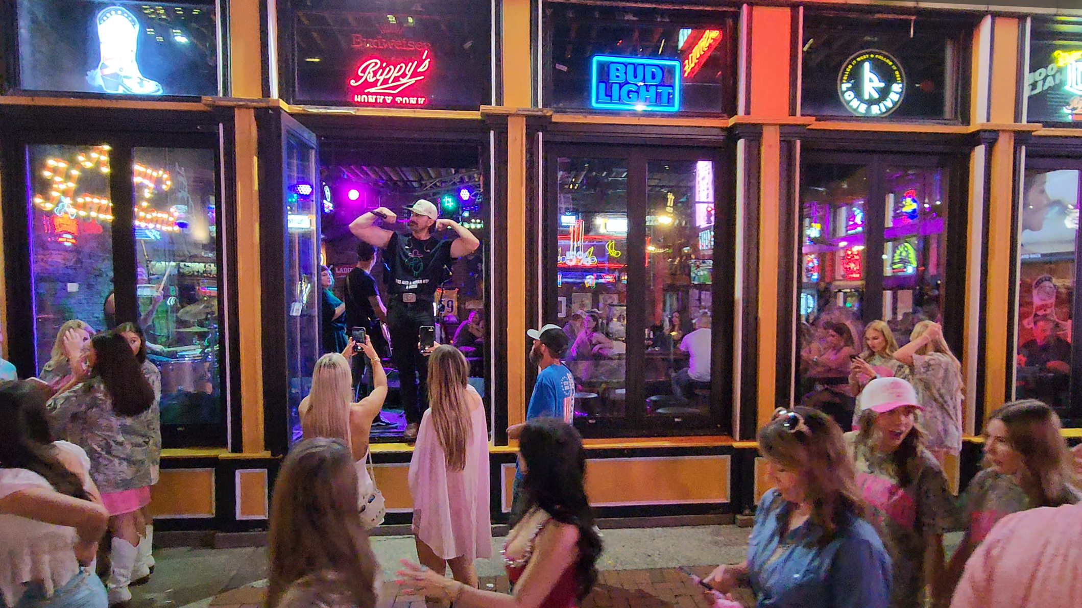 A live performer singing inside a Lower Broadway bar as visitors gather outside the open windows.